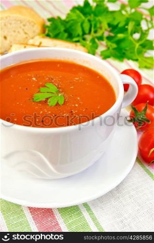 Tomato soup in a white cup and saucer, tomatoes, bread, parsley on a linen tablecloth background