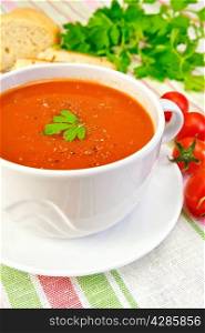 Tomato soup in a white cup and saucer, tomatoes, bread, parsley on a linen tablecloth background