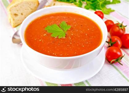 Tomato soup with peppers in white bowl on a saucer, tomatoes, bread, parsley on a linen tablecloth background