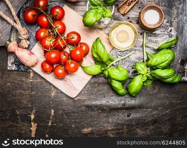 Tomatoes and basil with olive oil on wooden cutting board on rustic background, top view, border. Italian cooking concept.