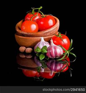 Tomatoes and garlic in wooden plate on black background.