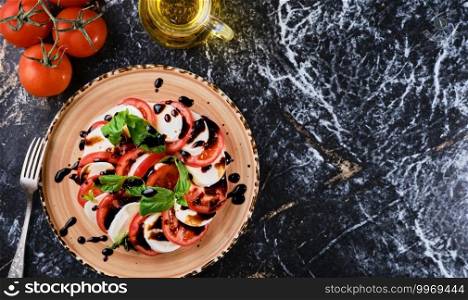 Tomatoes and mazzarella, Italian Caprese salad with tomatoes, mozzarella cheese, basil balsamic vinegar and olive oil. Dark marble background, top view, Vegetarian dish