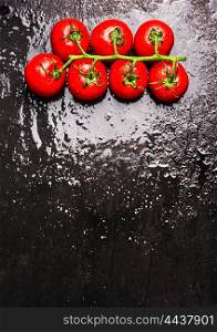tomatoes branch with water drops on wet dark slate, food background with cooking concept