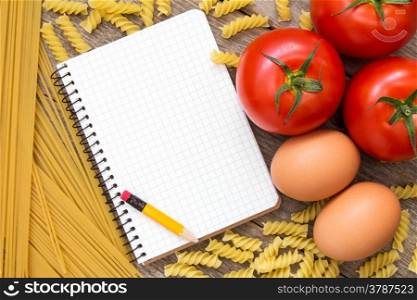 Tomatoes, eggs, uncooked pasta and blank recipe book