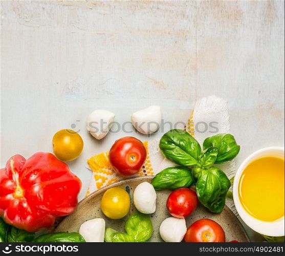 Tomatoes, mozzarella balls with basil leaves and oil in white bowl on rustic wooden background, top view, place for text