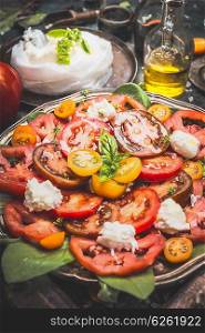 Tomatoes mozzarella salad on dark rustic kitchen table, close up