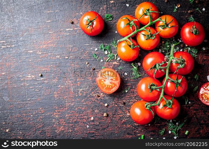 Tomatoes on a branch with pieces of greens and spices. Against a dark background. High quality photo. Tomatoes on a branch with pieces of greens and spices.