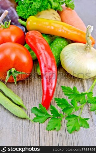 Tomatoes, peppers different, cucumbers, potatoes, carrots, bean pods, parsley, onions on a wooden boards background