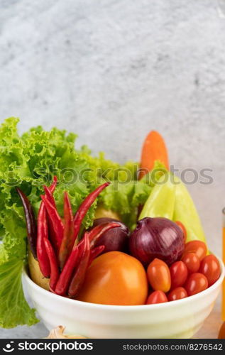 Tomatoes, red onions, bell peppers, carrots, and Chinese cabbage in a white cup on the cement floor.