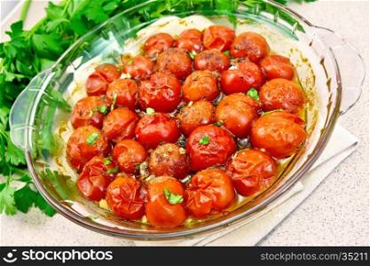 Tomatoes small baked with spices, garlic and salt, parsley in a glass pan on a napkin against the background of the stone table