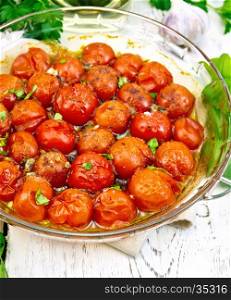 Tomatoes small baked with spices, garlic and salt, parsley in a glass pan on the background light wooden boards