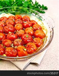 Tomatoes small baked with spices, garlic and salt, parsley in a glass pan on a napkin on a background of a granite table