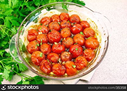 Tomatoes small baked with spices, garlic and salt, parsley in a glass pan on a background of stone table