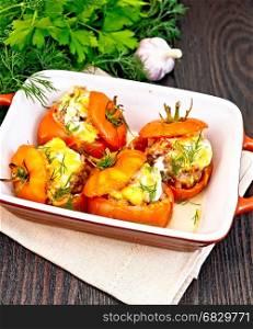 Tomatoes stuffed with meat and rice with cheese in a brazier on a light napkin, parsley, dill and garlic on a background of a dark wooden board
