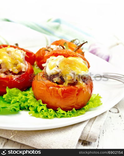 Tomatoes stuffed with meat and rice with cheese on lettuce in a plate on a napkin, fork against a light wooden board