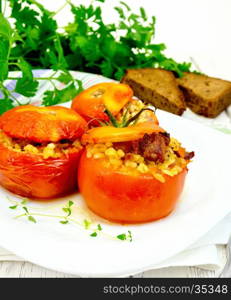 Tomatoes stuffed with meat and steamed wheat bulgur, a sprig of thyme in a white plate, napkin, fork, bread and parsley on the background light wooden boards