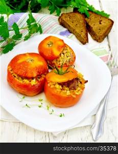 Tomatoes stuffed with meat and steamed wheat bulgur, a sprig of thyme in a white plate, napkin, fork, bread and parsley on a wooden board background