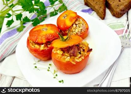Tomatoes stuffed with meat and steamed wheat bulgur, a sprig of thyme in a plate, napkin, fork, bread and parsley on a wooden board background