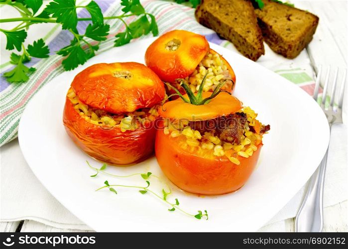 Tomatoes stuffed with meat and steamed wheat bulgur in a plate, napkin, fork, bread and parsley on the background light wooden boards. Tomatoes stuffed with bulgur in plate on table