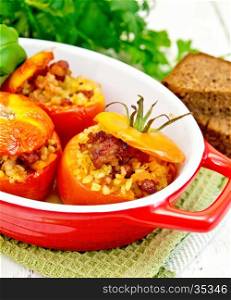 Tomatoes stuffed with meat and steamed wheat bulgur in a roasting pan on a napkin, bread and parsley on a wooden board background