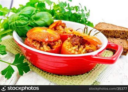 Tomatoes stuffed with meat and steamed wheat bulgur in a roasting pan on a napkin, bread, parsley and basil on the background light wooden boards