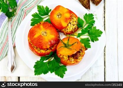 Tomatoes stuffed with meat and steamed wheat bulgur in a white plate, napkin, fork, bread and parsley on a background of wooden boards on top