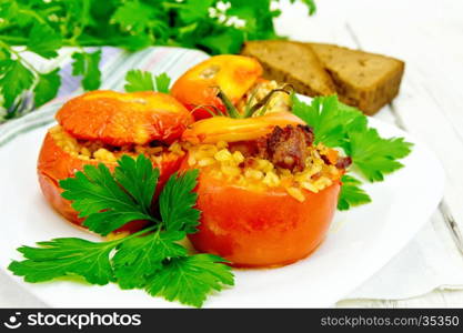 Tomatoes stuffed with meat and steamed wheat bulgur, parsley in a white plate, napkin, fork and bread on the background light wooden boards