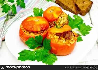 Tomatoes stuffed with meat and steamed wheat bulgur, parsley in a white plate, napkin, fork and bread on a wooden boards background