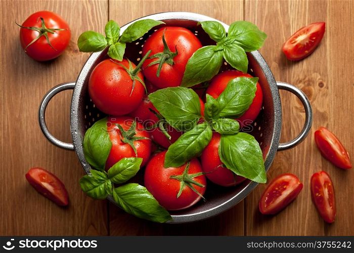 Tomatoes with basil in colander on wooden table background. Food composition. Top view