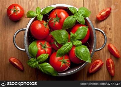 Tomatoes with basil in colander on wooden table background. Food composition. Top view