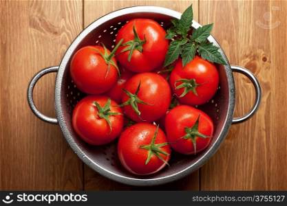 Tomatoes with green leaf in colander on wooden table background. Top view shot