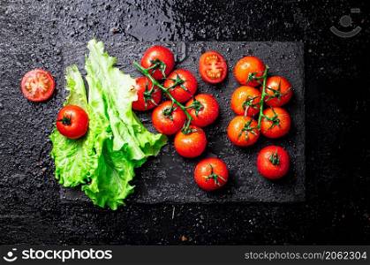 Tomatoes with lettuce leaves on a stone board. On a black background. High quality photo. Tomatoes with lettuce leaves on a stone board.