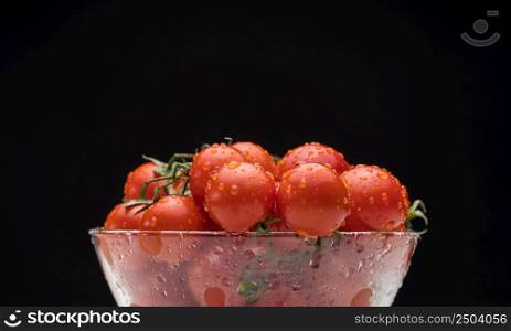 tomatoes with water drops in a glassware on a black background, horizontal plane. tomatoes in a glass bowl