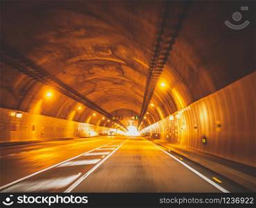Toned blurred photo of cars driving fast in long tunnel under mountain. Toned blurred image of cars driving fast in long tunnel under mountain