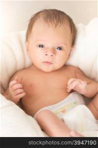 Toned closeup portrait of cute baby boy with blue eyes lying on cushions