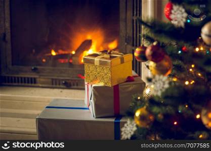 Toned image of beautiful Christmas tree and stack of presents in front of burning fireplace