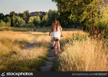 Toned image of beautiful girl riding bike at fields at sunset