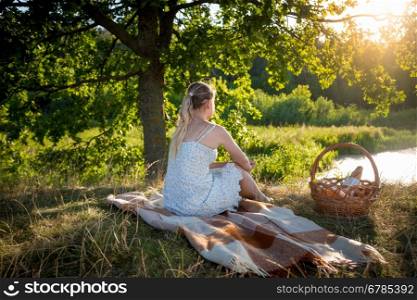 Toned image of beautiful lonely woman relaxing under big tree and looking at sunset