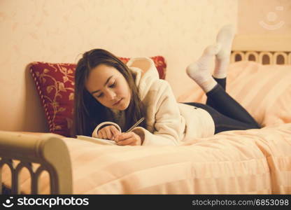 Toned image of beautiful teenage girl lying on bed with her private diary