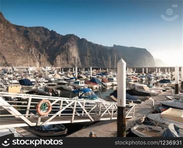 Toned image of big harbour with moored motor boats and yachts in the ocean against high cliffs and mountains. Toned photo of big harbour with moored motor boats and yachts in the ocean against high cliffs and mountains