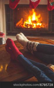Toned image of couple wearing woolen socks relaxing at burning fireplace at Christmas