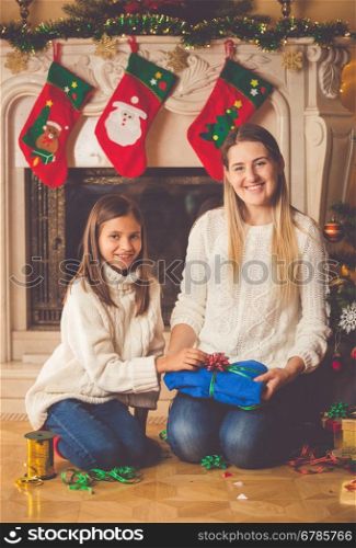 Toned image of happy young mother and daughter packing Christmas presents on floor at living room