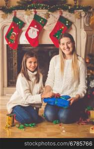 Toned image of happy young mother and daughter packing Christmas presents on floor at living room
