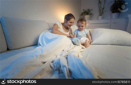 Toned image of mother playing with baby son on bed at night