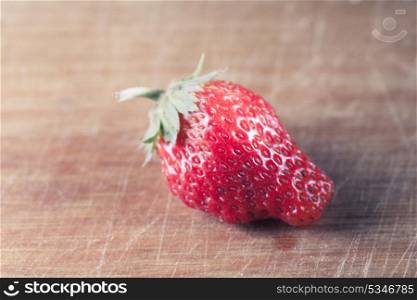 toned image of the one strawberry on the wooden plank, side view