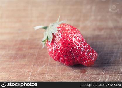 toned image of the one strawberry on the wooden plank, side view