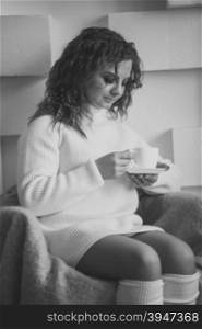Toned monochrome portrait of cute woman in sweater looking at cup of tea