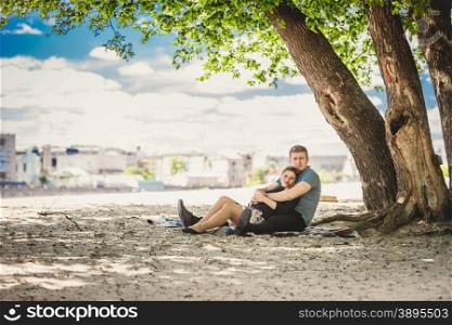 Toned photo of beautiful couple in love relaxing under tree on riverbank