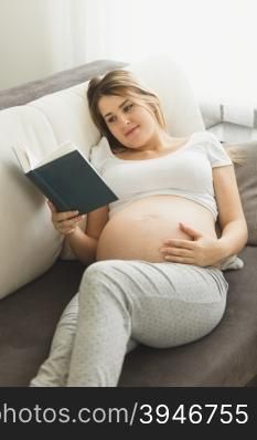 Toned photo of beautiful pregnant woman lying on sofa and reading book
