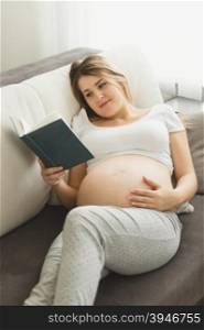 Toned photo of beautiful pregnant woman lying on sofa and reading book